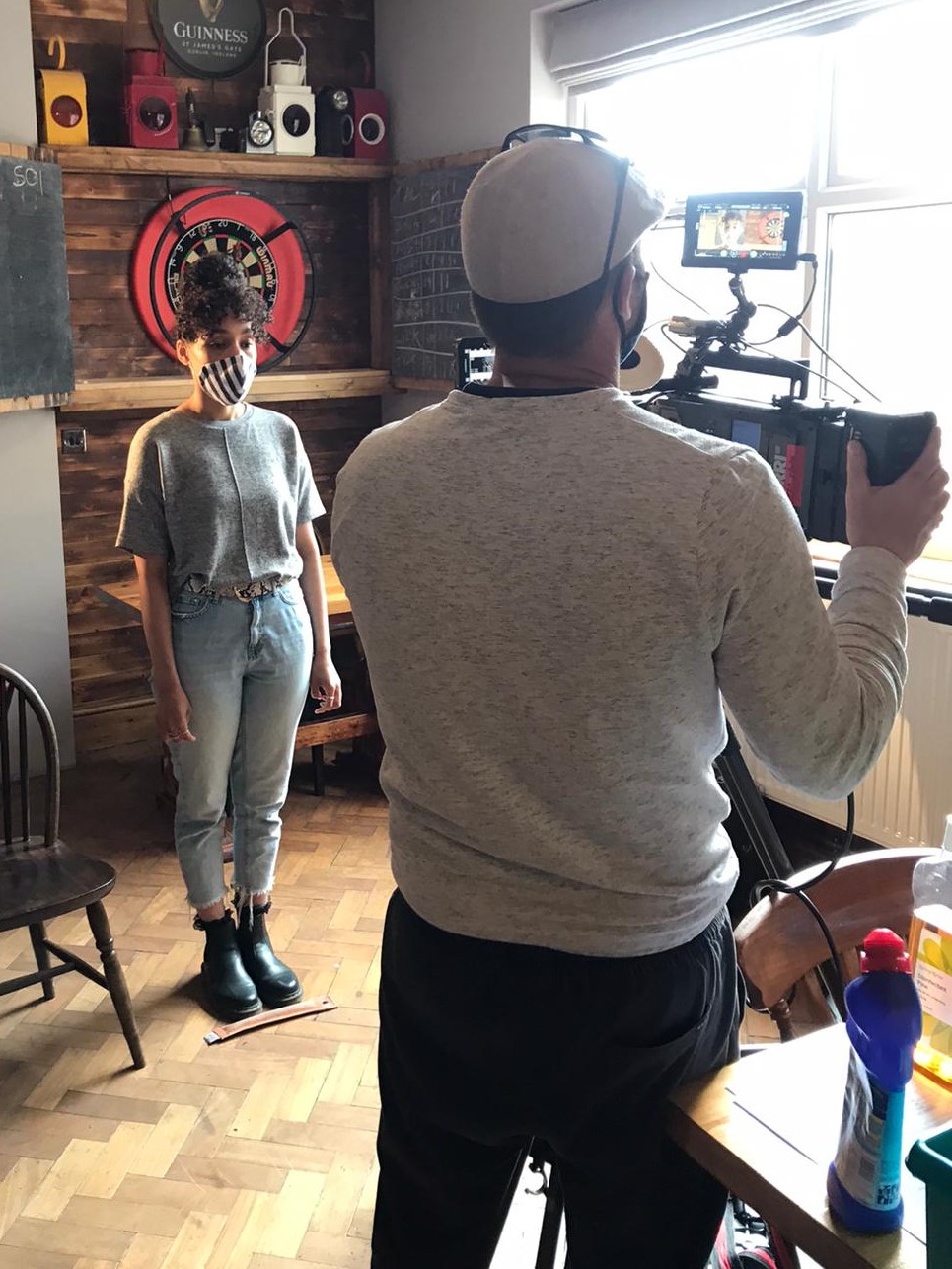 behind the scenes of a short film shoot, featuring a person posing by a dartboard in a pub for someone filming.