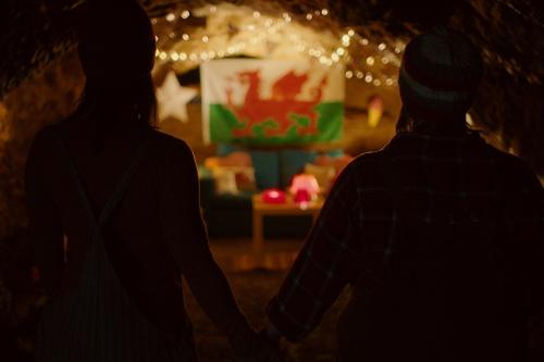 still from jelly featuring two people standing in a cave in front of a welsh flag and holding hands