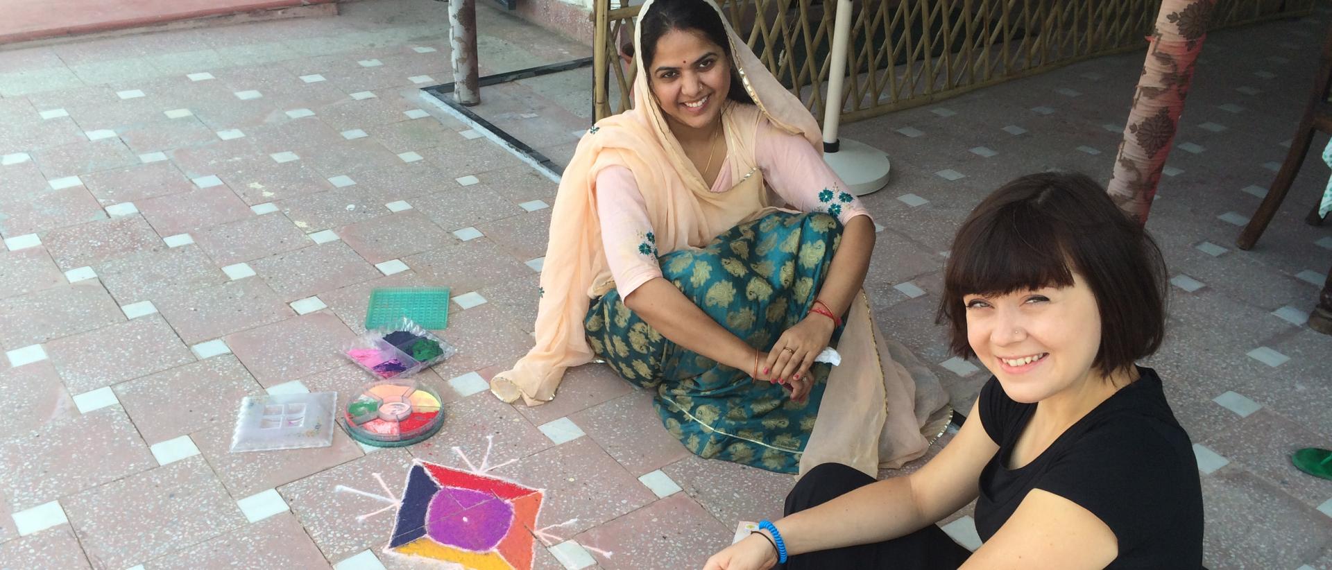 two people sitting on the floor creating rangoli art