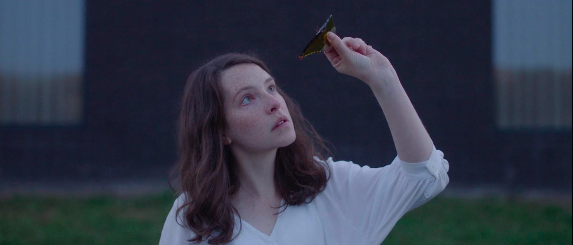 a still from Gwledd / The Feast featuring Annes Elwy holding a piece of broken wine bottle up to the light to look through it
