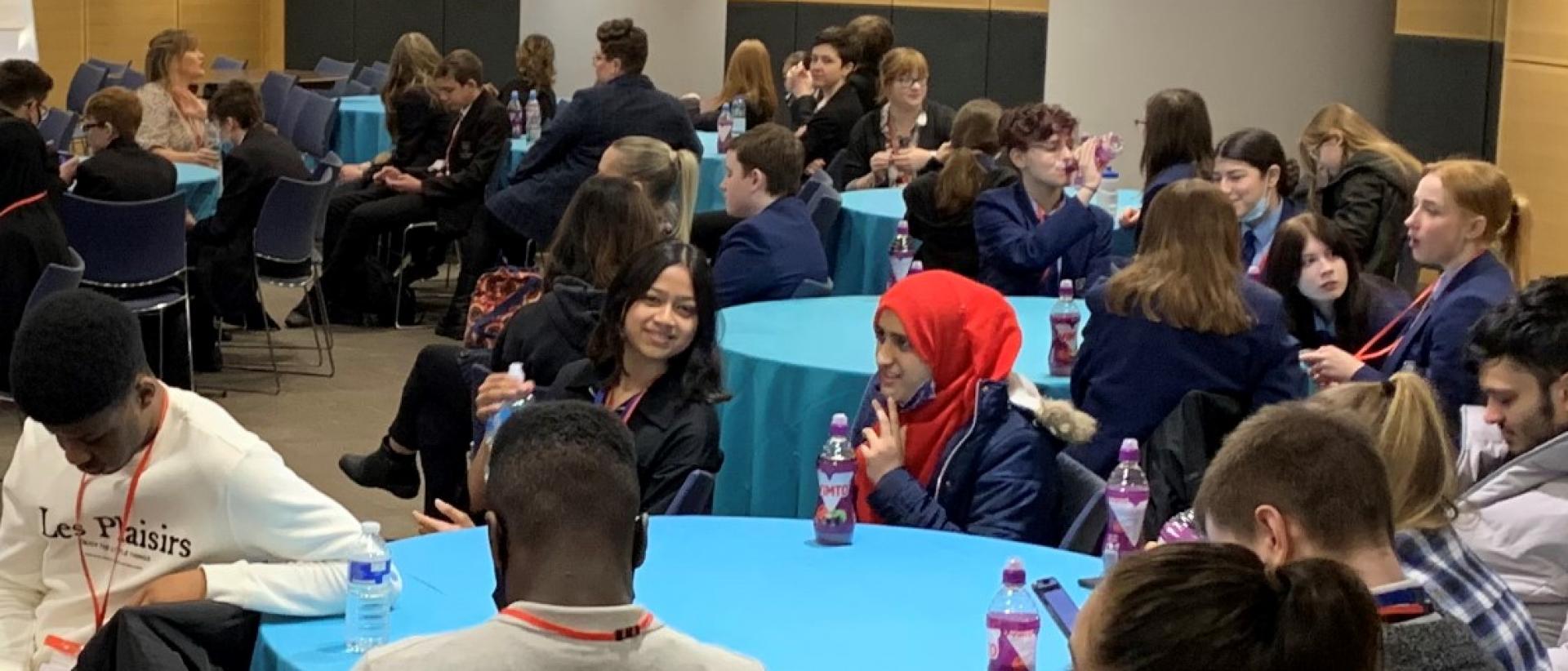a photo of young people sitting around circular tables in a conference hall