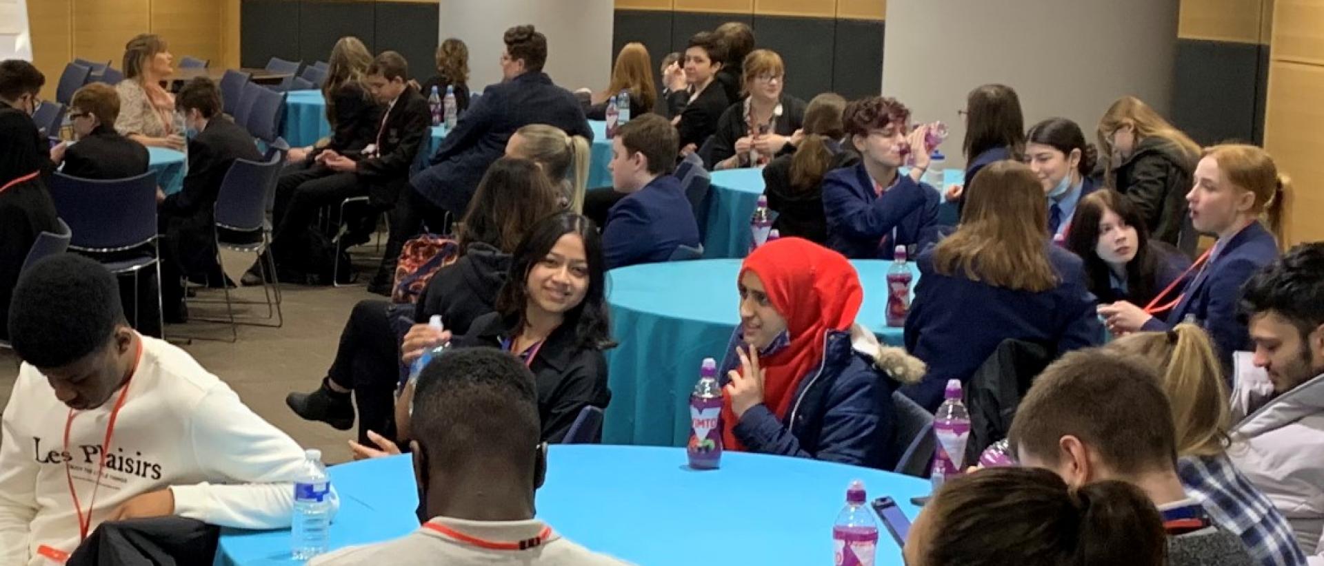 a photo of young people sitting around circular tables in a conference hall