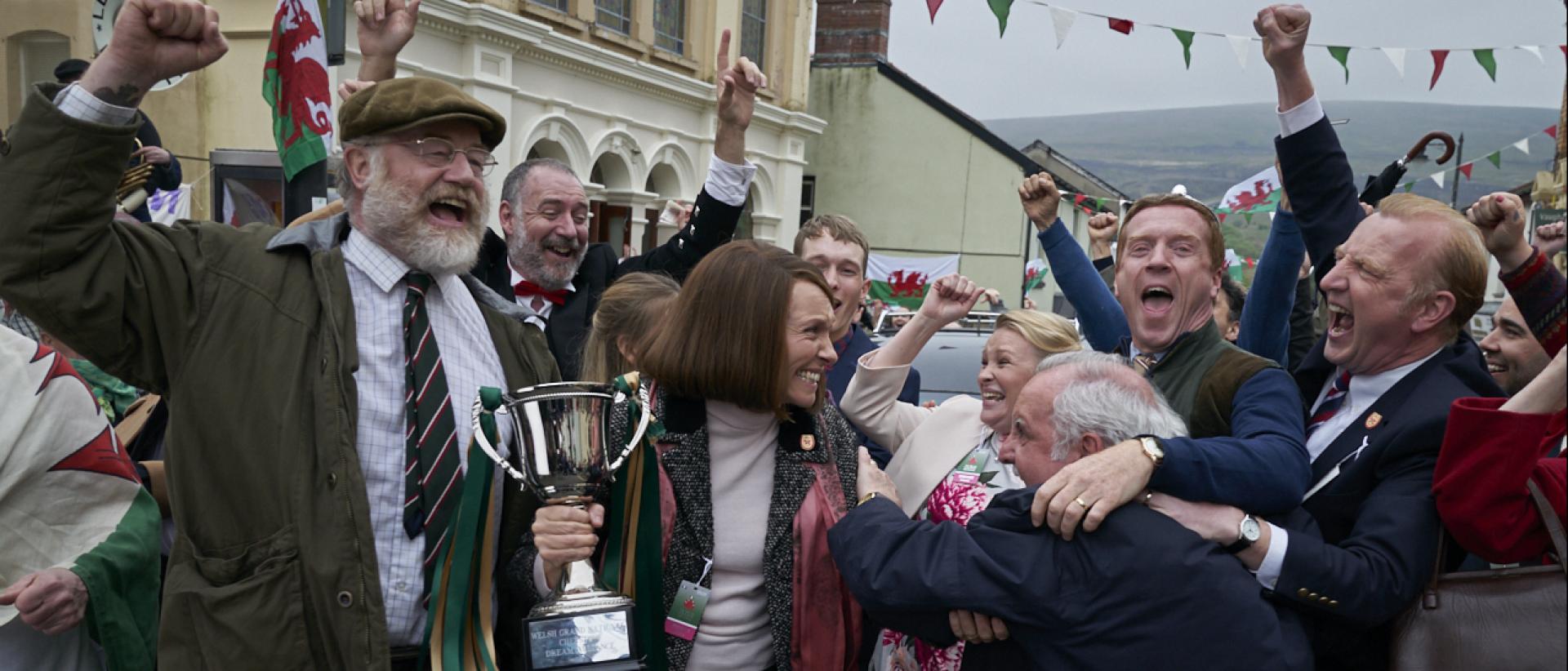still from dream horse featuring toni collette holding a trophy and celebrating during a street party parade