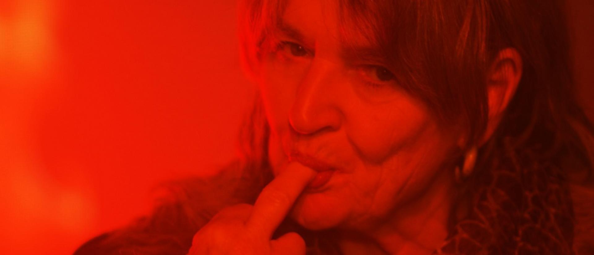 still from geronimo featuring a woman in red light with the tip of her finger in her mouth
