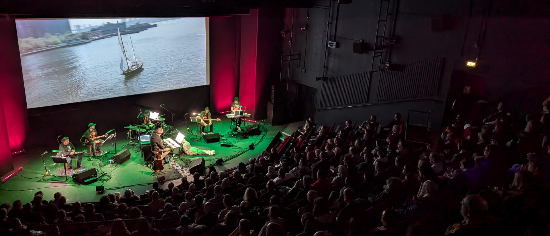 photo of a full auditorium at aberystwyth arts centre as a band plays along live with a film on the screen
