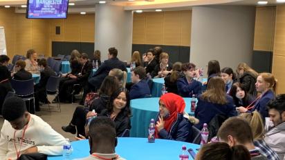 a photo of young people sitting around circular tables in a conference hall