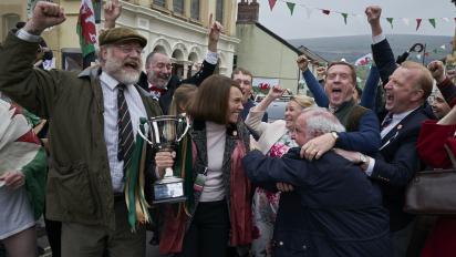 still from dream horse featuring toni collette holding a trophy and celebrating during a street party parade