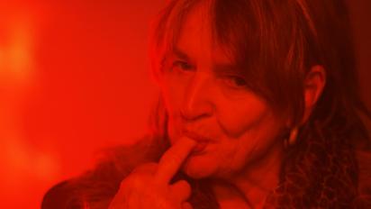 still from geronimo featuring a woman in red light with the tip of her finger in her mouth