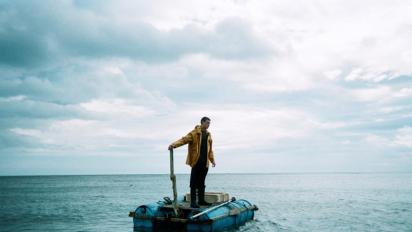 still from for those in peril featuring a man standing on a dinghy in the ocean