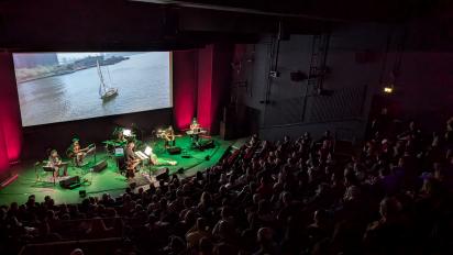 photo of a full auditorium at aberystwyth arts centre as a band plays along live with a film on the screen